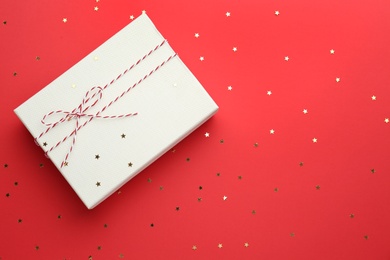 Photo of Gift box and confetti stars on red background, flat lay. Christmas celebration