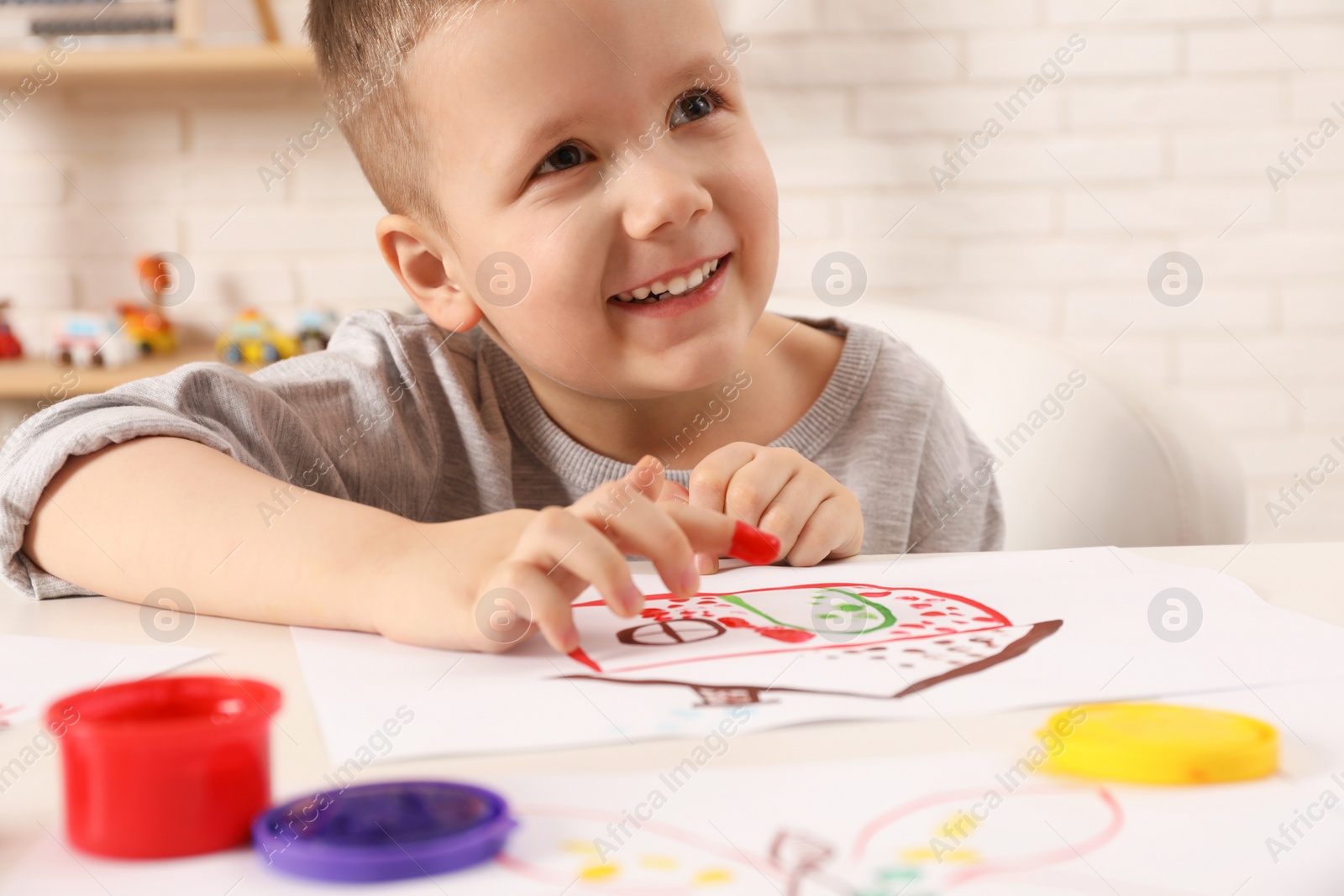 Photo of Little boy painting with finger at white table indoors