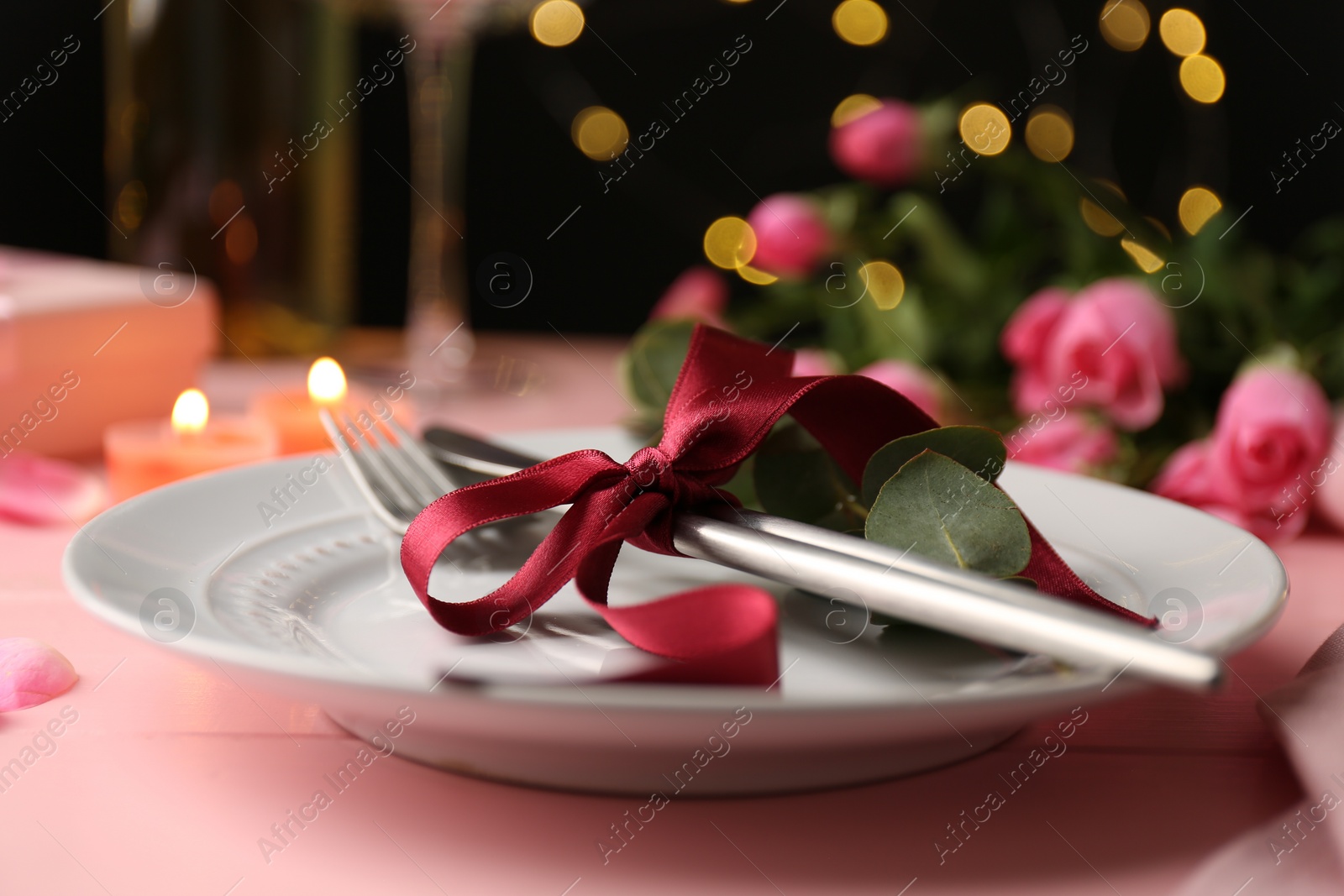 Photo of Place setting with roses and candles on pink table, closeup. Romantic dinner