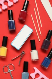 Photo of Nail polishes and set of pedicure tools on red background, flat lay