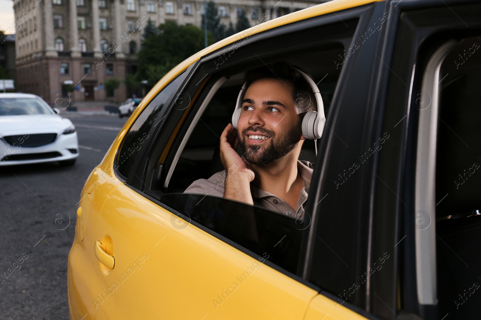 Photo of Handsome young man with headphones in taxi outdoors