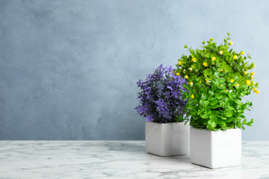 Photo of Artificial plants in flower pots on white marble table. Space for text