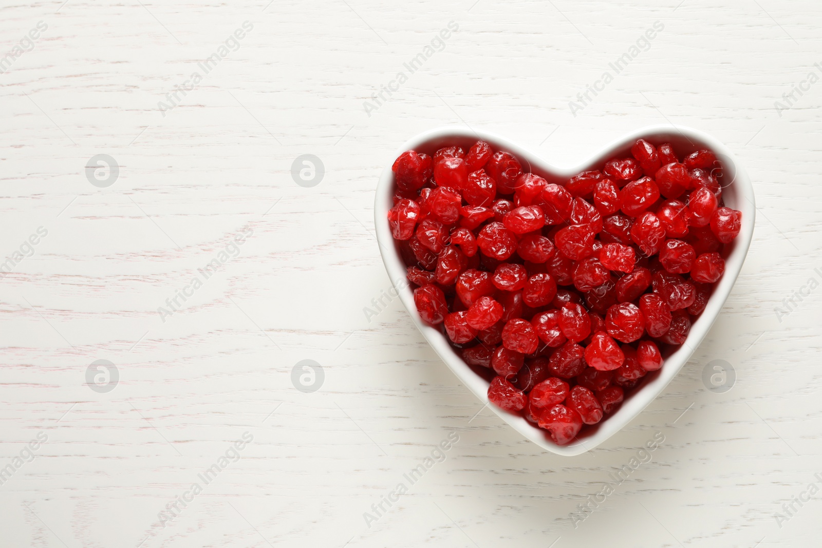 Photo of Heart shaped bowl of sweet cherries on wooden background, top view with space for text. Dried fruit as healthy snack