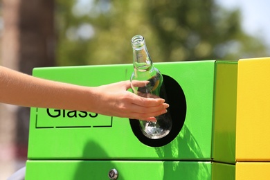 Woman throwing glass bottle into sorting bin on city street, closeup. Recycling waste