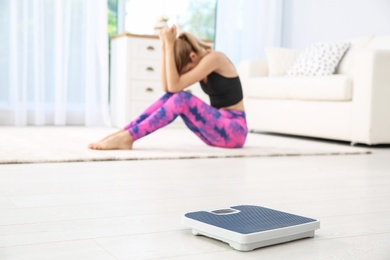 Photo of Scales on floor and sad young woman at home. Weight loss motivation