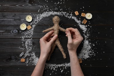 Photo of Woman stabbing voodoo doll with pins at wooden table, top view