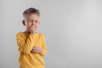 Sick boy coughing on gray background, space for text. Cold symptoms