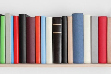 Photo of Wooden shelf with many hardcover books on white wall
