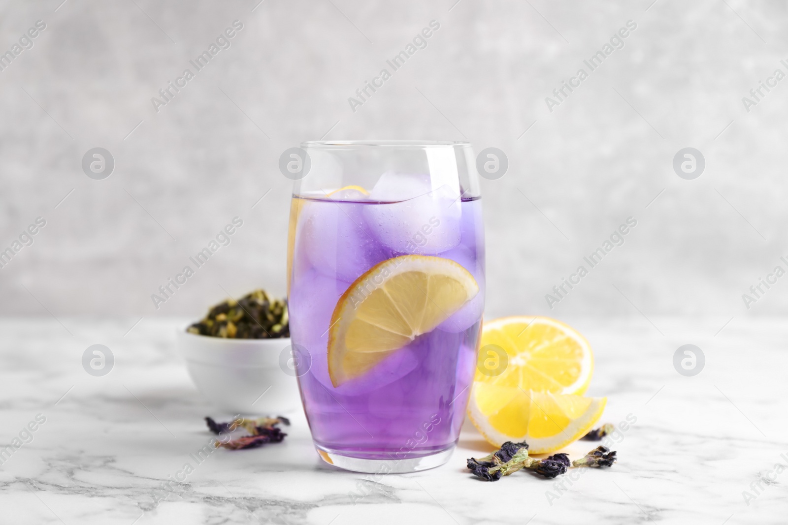 Photo of Glass of organic blue Anchan with lemon and ice on white marble table. Herbal tea