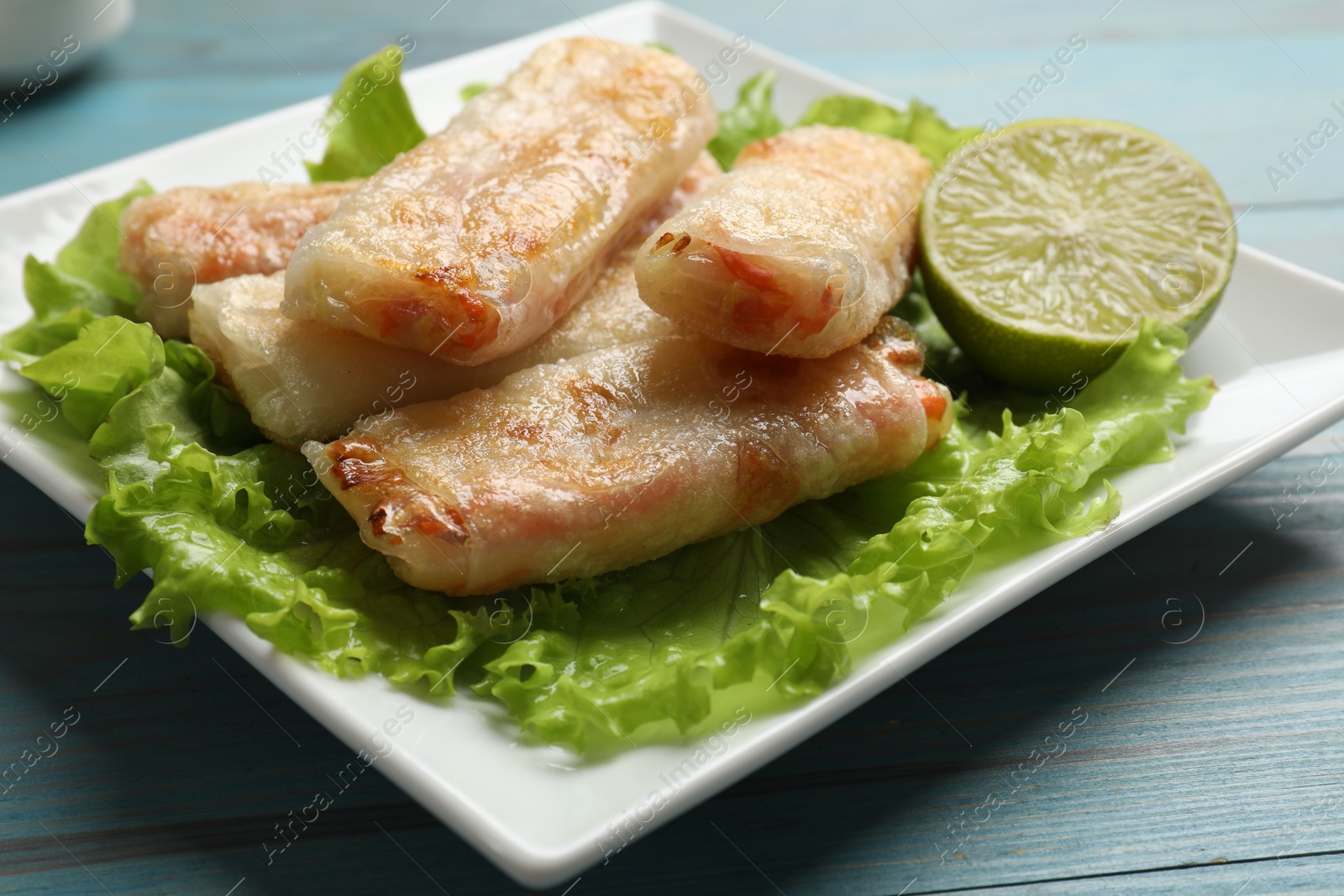 Photo of Delicious fried spring rolls on light blue wooden table, closeup