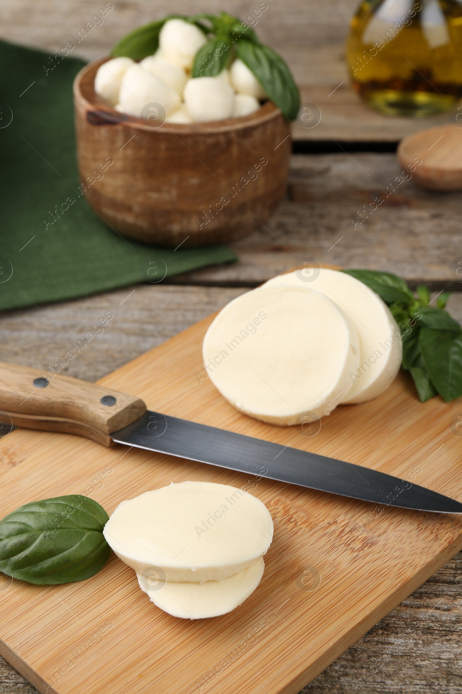 Photo of Board with tasty mozzarella slices, basil leaves and knife on wooden table