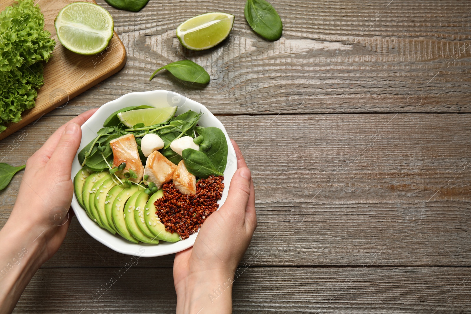 Photo of Woman holding bowl of delicious avocado salad with chicken at wooden table, top view. Space for text