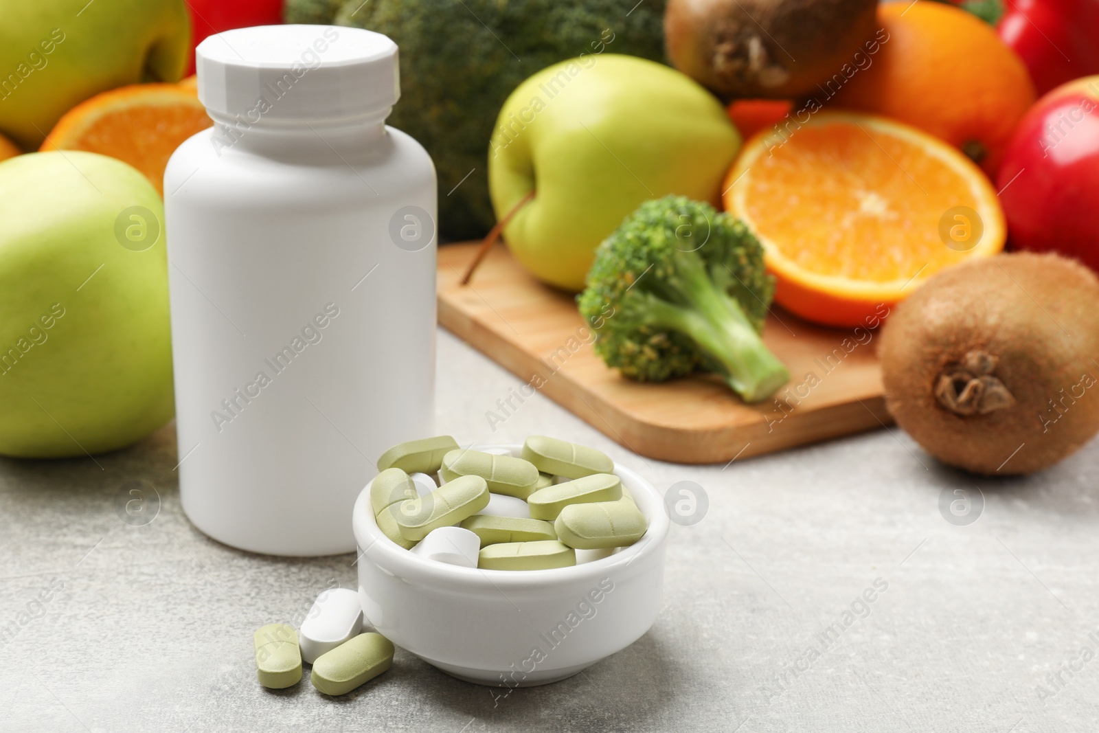 Photo of Dietary supplements. Plastic bottle, pills in bowl and food products on grey table