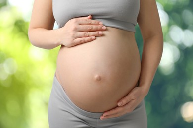 Young pregnant woman touching her belly outdoors, closeup