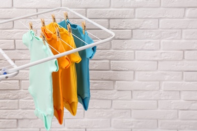 Photo of Different cute baby onesies hanging on clothes line near brick wall, space for text. Laundry day