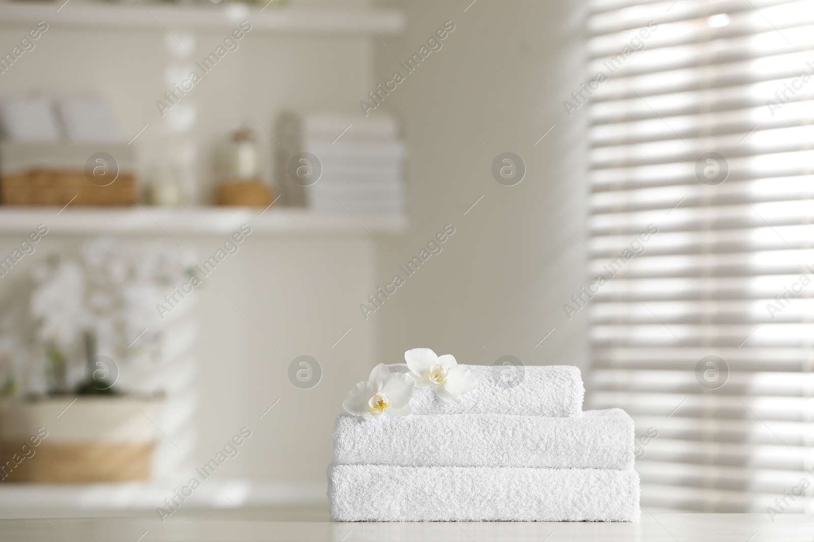 Photo of Stack of clean soft towels with orchid flowers on white table indoors