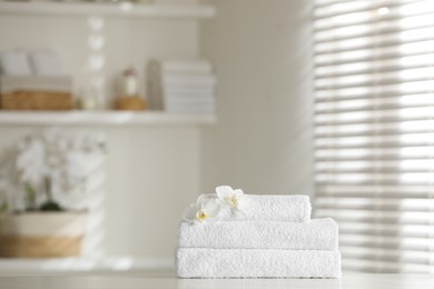 Photo of Stack of clean soft towels with orchid flowers on white table indoors