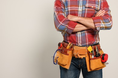 Photo of Professional builder with tool belt on light background, closeup. Space for text