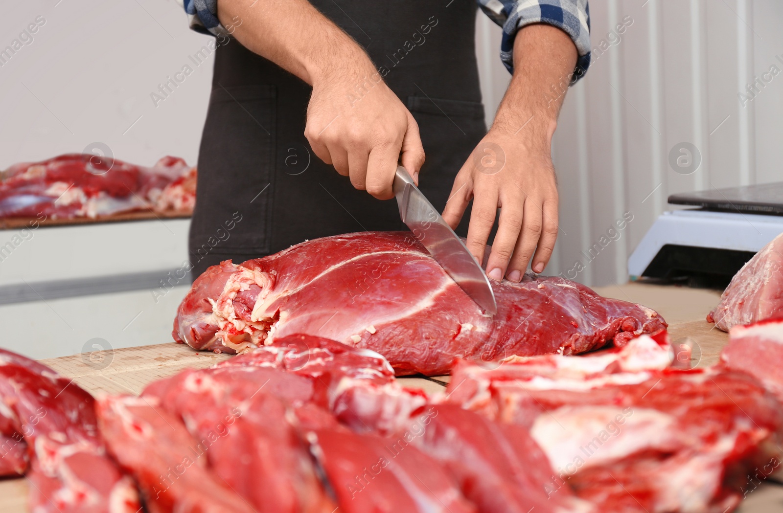 Photo of Butcher cutting fresh raw meat on counter in shop, closeup