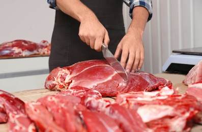 Photo of Butcher cutting fresh raw meat on counter in shop, closeup