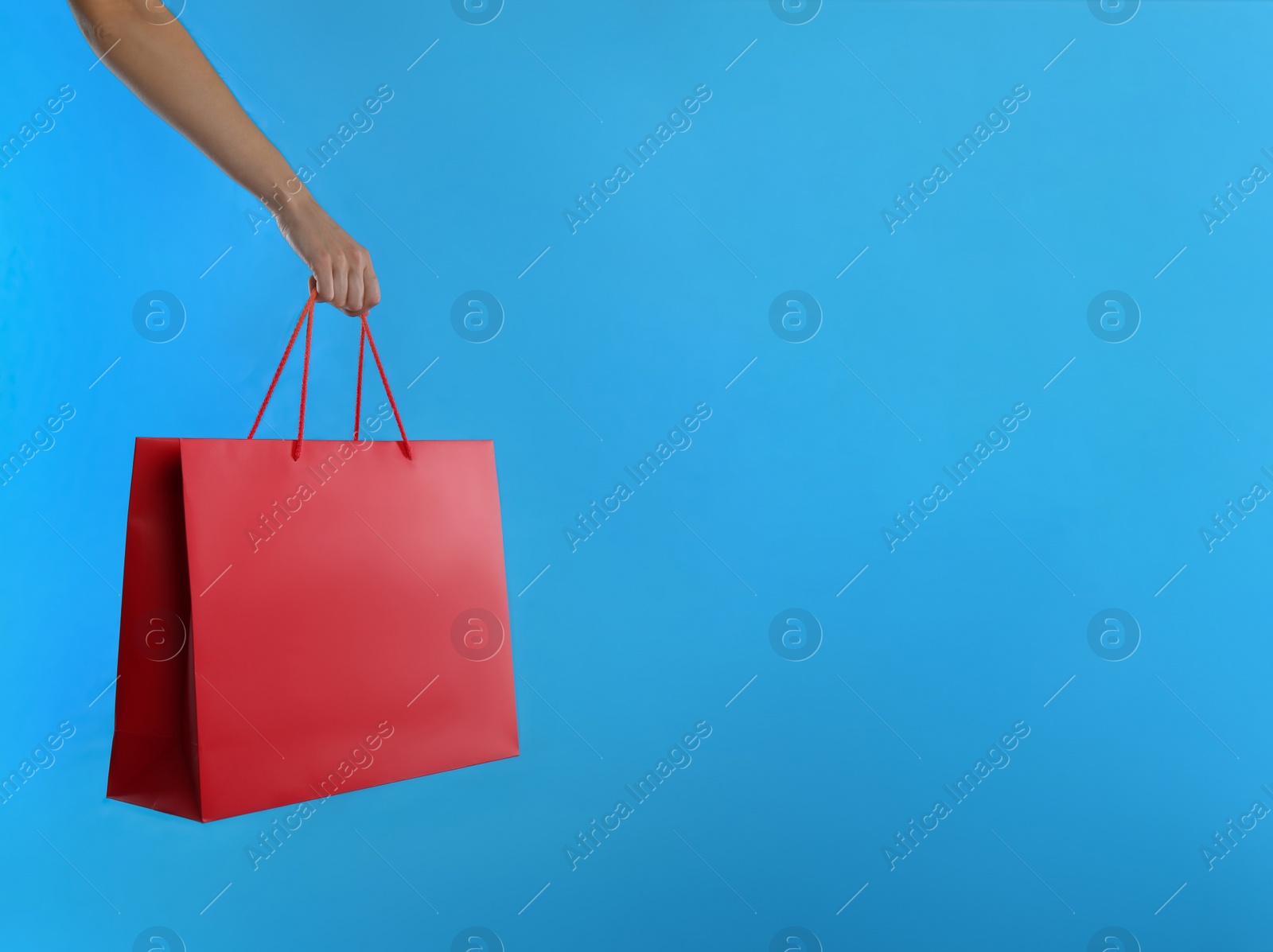 Photo of Woman with paper shopping bag on light blue background, closeup. Space for text