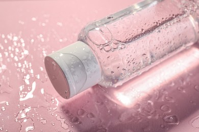 Photo of Wet bottle of micellar water on pink background, closeup