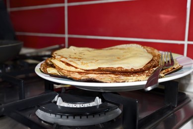 Photo of Plate of freshly made crepes with fork on stove in kitchen, closeup