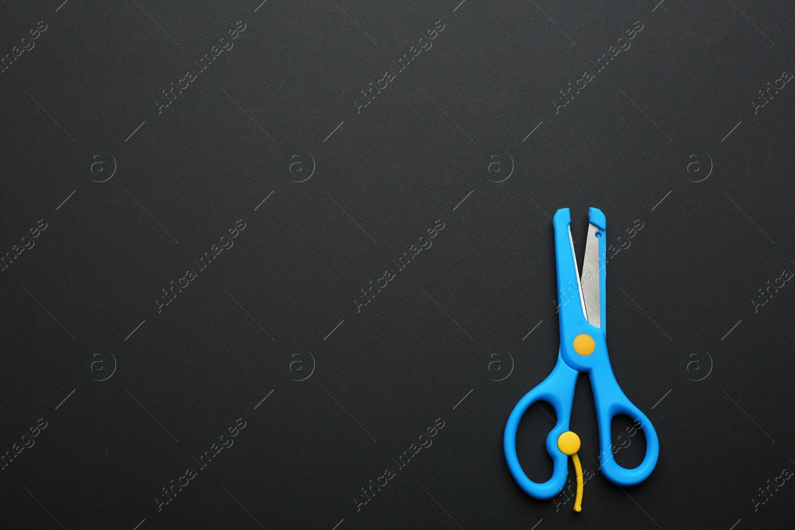 Photo of Pair of training scissors on dark background, top view. Space for text