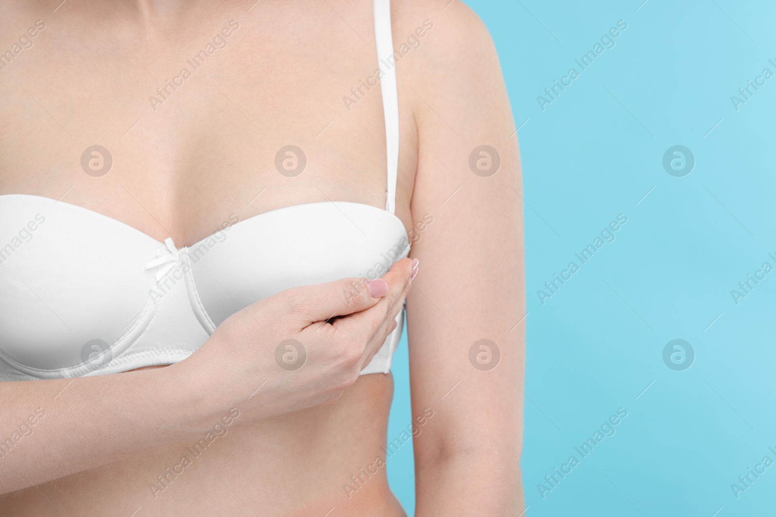 Photo of Mammology. Young woman doing breast self-examination on light blue background, closeup. Space for text