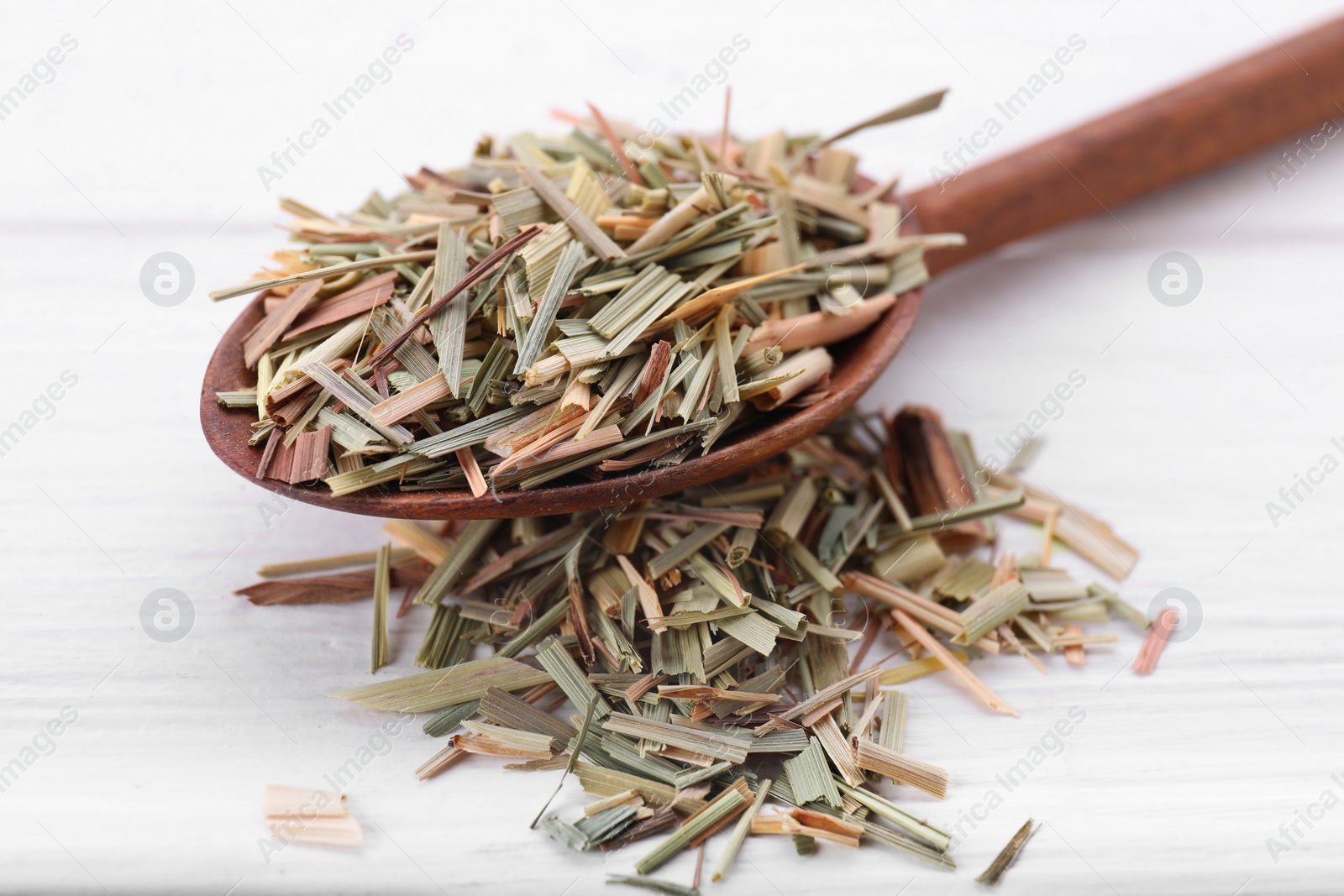 Photo of Spoon with aromatic dried lemongrass on white wooden table, closeup