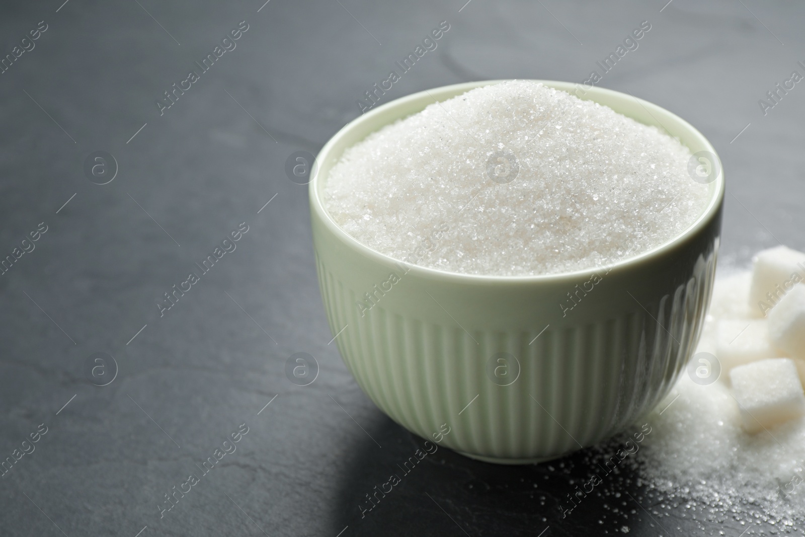 Photo of Granulated sugar in bowl on dark table