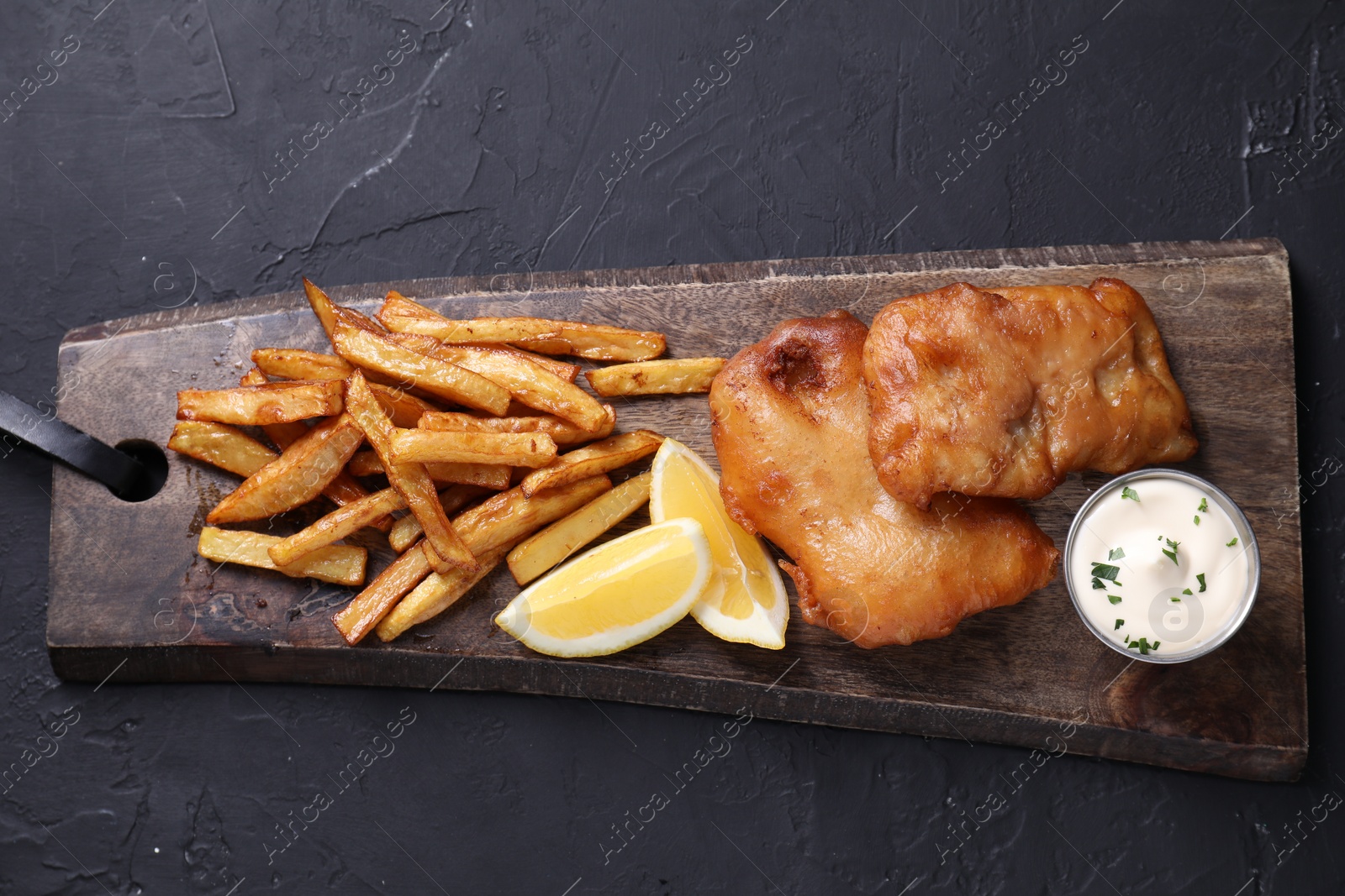 Photo of Tasty fish, chips, lemon and sauce on black table, top view