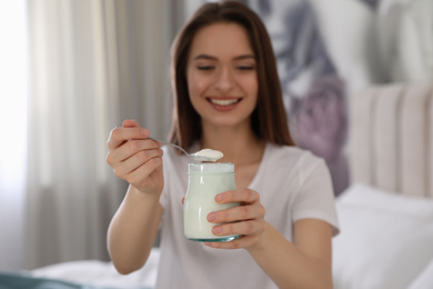 Photo of Young attractive woman with tasty yogurt in bedroom, focus on hands