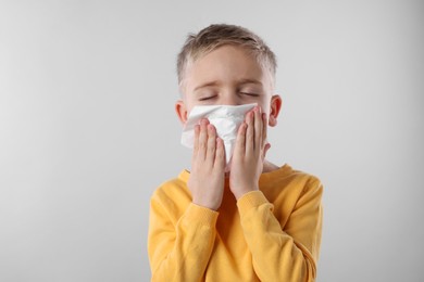 Sick boy with tissue coughing on gray background. Cold symptoms