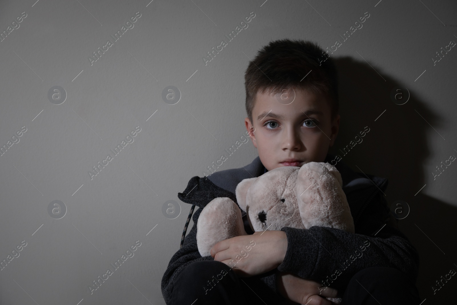 Photo of Sad little boy with teddy bear near beige wall, space for text. Domestic violence concept