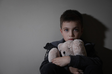 Photo of Sad little boy with teddy bear near beige wall, space for text. Domestic violence concept