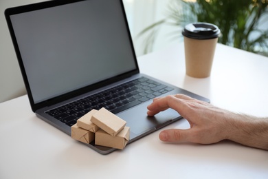 Photo of Internet shopping. Small boxes near man using laptop at table indoors, closeup