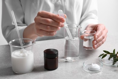 Scientist making cosmetic product at grey table in laboratory, closeup