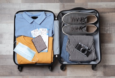 Photo of Open suitcase with passport, tickets and protective mask on wooden floor, top view. Travel during quarantine
