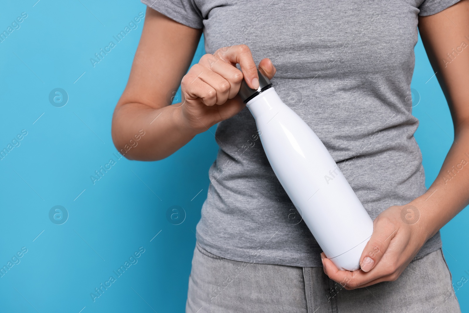 Photo of Woman holding thermo bottle on light blue background, closeup. Space for text
