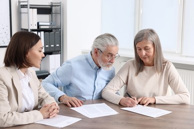 Photo of Elderly couple consulting insurance agent about pension plan at wooden table indoors
