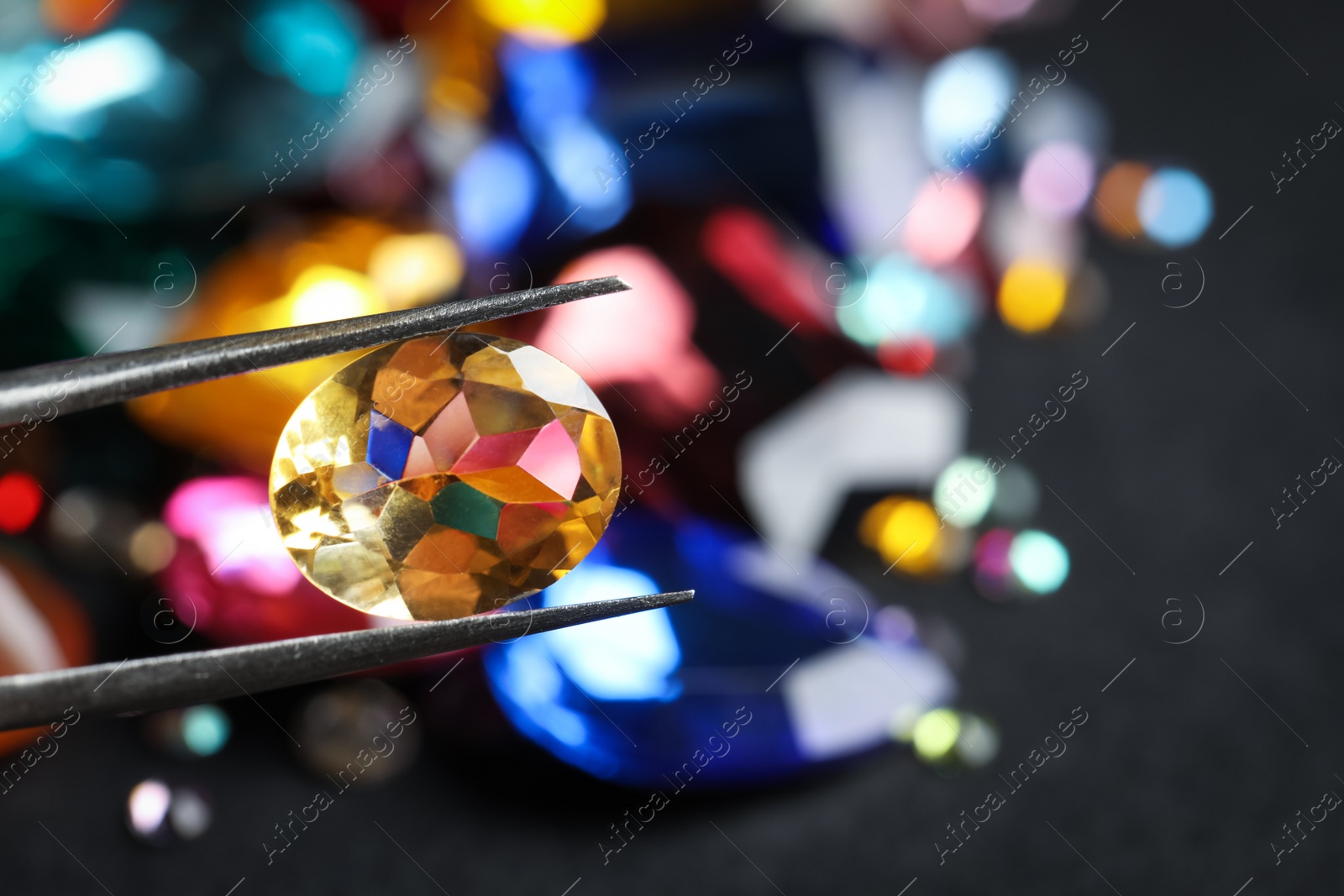 Photo of Tweezers with beautiful gemstone on blurred background, closeup. Space for text