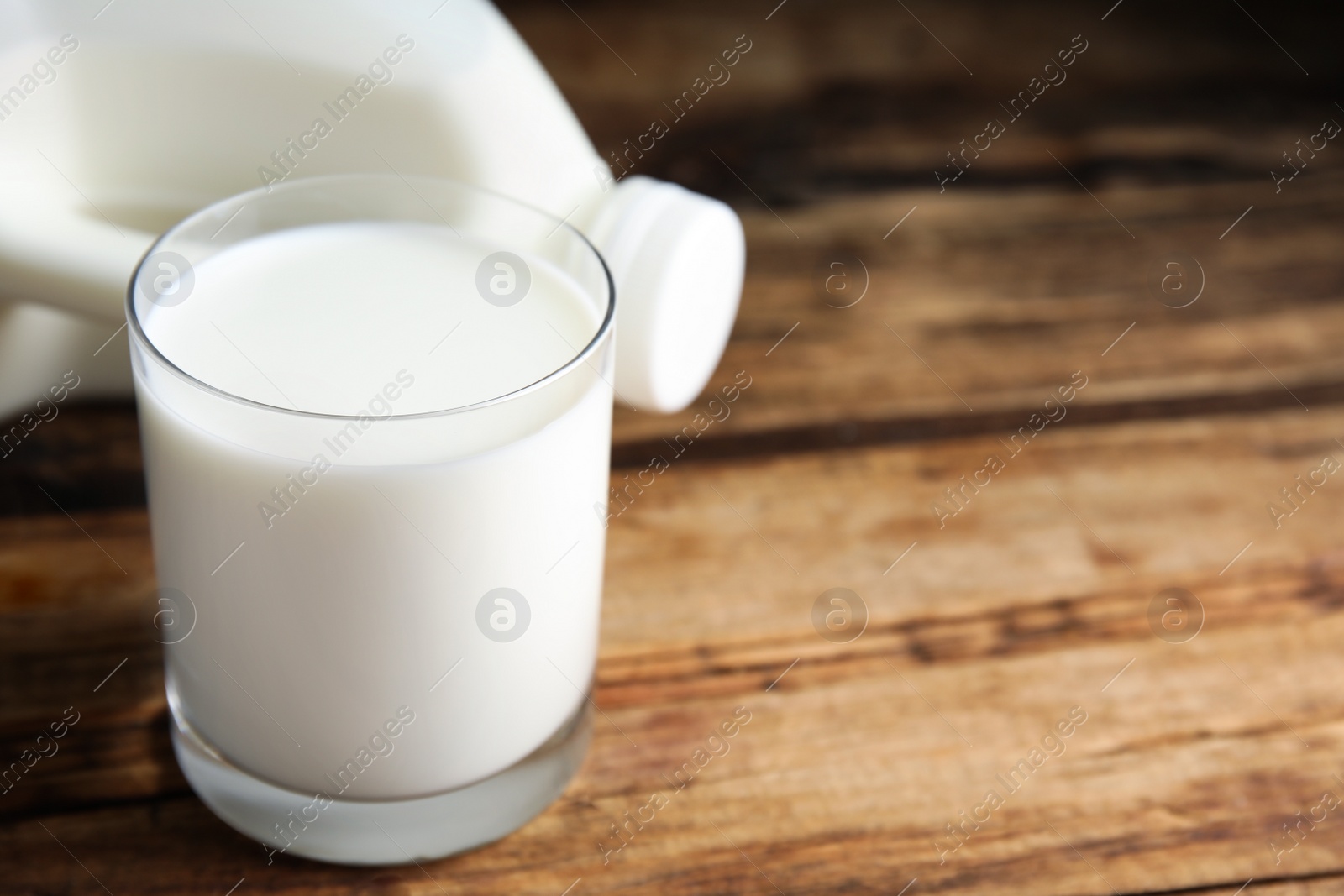 Photo of Glass of milk near gallon bottle on wooden table, closeup. Space for text