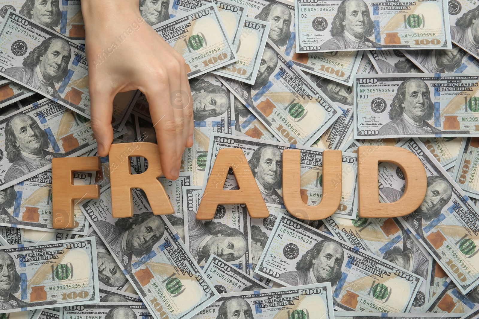 Photo of Woman making word Fraud with wooden letters on pile of dollar banknotes, top view