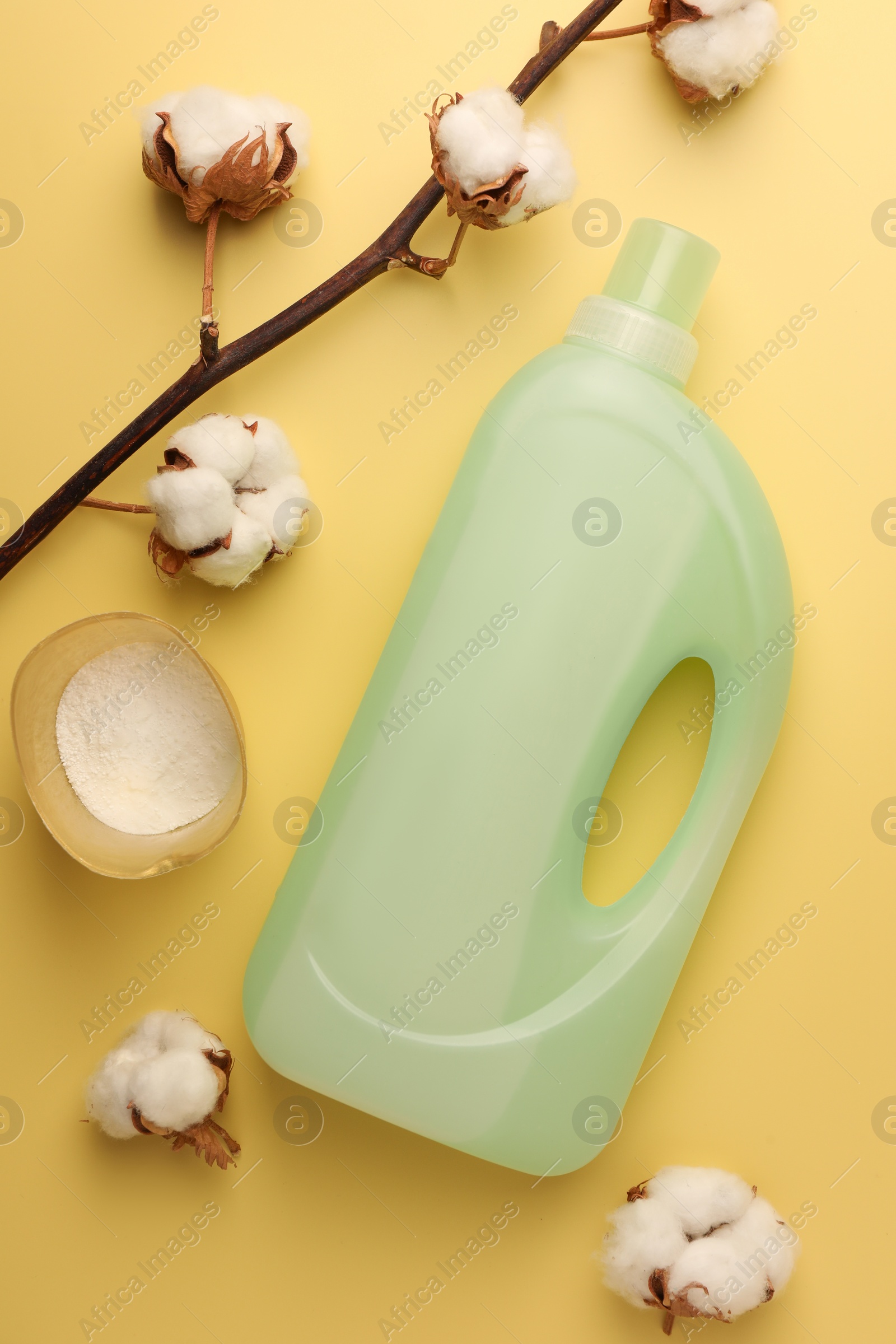 Bottle of fabric softener, detergent powder and cotton flowers on pale yellow background, flat lay Photo of Bottle of fabric softener, detergent powder and cotton flowers on pale yellow background, flat lay