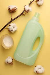 Photo of Bottle of fabric softener, detergent powder and cotton flowers on pale yellow background, flat lay