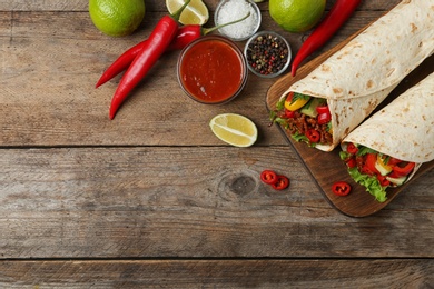 Board with delicious meat tortilla wraps on wooden table, flat lay. Space for text