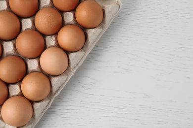 Photo of Raw chicken eggs on white wooden table, top view. Space for text