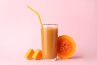 Tasty pumpkin juice in glass and cut pumpkin on pink background