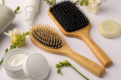 Wooden hairbrushes, different cosmetic products and beautiful flowers on white background